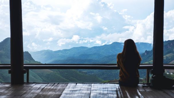 Rear view image of a female traveler sitting and looking at a beautiful mountain and nature view - Foto, Imagen