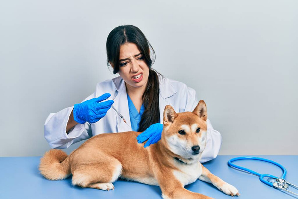 Schöne hispanische Tierärztin setzt Impfung Welpen Hund ahnungslosen und verwirrten Ausdruck. Zweifelhaftes Konzept.  - Foto, Bild