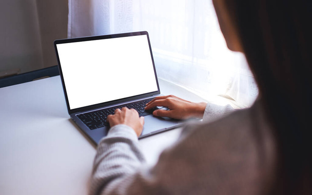 Mockup-Bild einer Geschäftsfrau, die eine Laptop-Computertastatur mit leerem weißen Desktop-Bildschirm auf dem Tisch benutzt und tippt - Foto, Bild