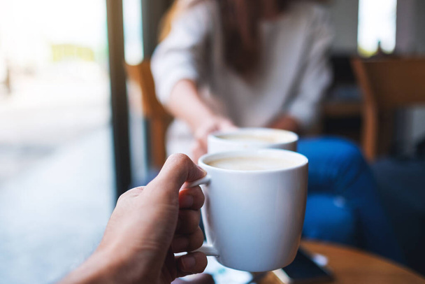 Closeup image of man and woman clinking white coffee mugs in cafe - Foto, imagen