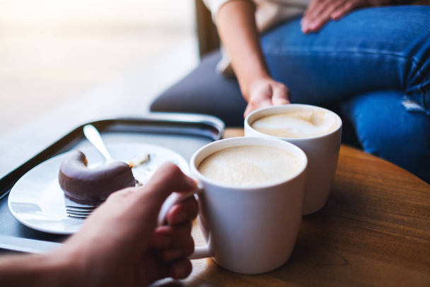 Closeup image of two people clink white coffee mugs on wooden table in cafe - Foto, imagen