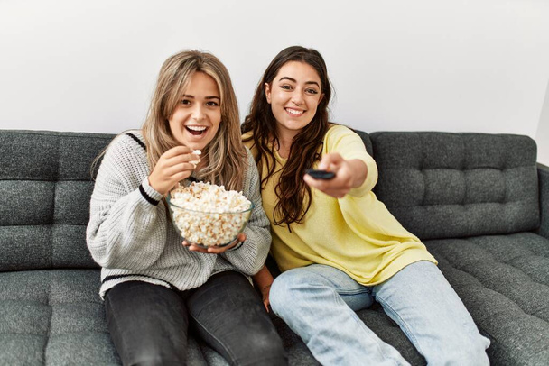 jong paar kijken film en het eten van popcorn zitten op de bank thuis. - Foto, afbeelding