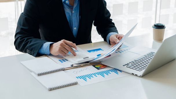 Un homme d'affaires ou un comptable tenant un stylo et un tableau analytique calcule le budget de l'entreprise et le taux de roulement de la planification financière avec le rapport graphique et utilise l'ordinateur portable pour l'analyse des données. - Photo, image