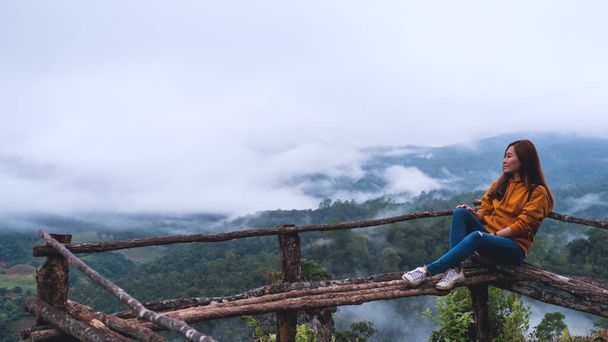 霧の日に美しい山と自然を眺めながら座っている女性旅行者の肖像画 - 写真・画像