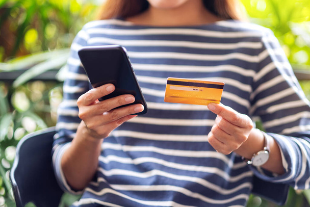 Μια γυναίκα που κατέχει πιστωτική κάρτα και δείχνει στο κινητό τηλέφωνο για την αγορά και ψώνια σε απευθείας σύνδεση  - Φωτογραφία, εικόνα