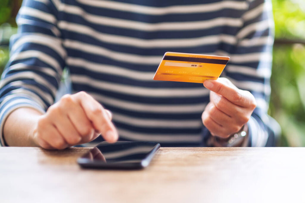 Uma mulher segurando cartão de crédito e apontando para o telefone celular para compra e compras online
  - Foto, Imagem
