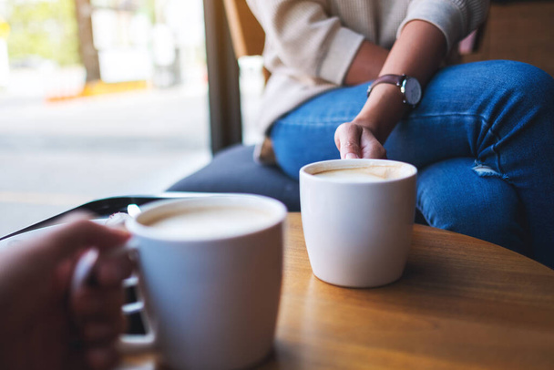 Imagen de cerca de dos personas sosteniendo tazas de café blanco para beber en la mesa de madera en la cafetería - Foto, Imagen