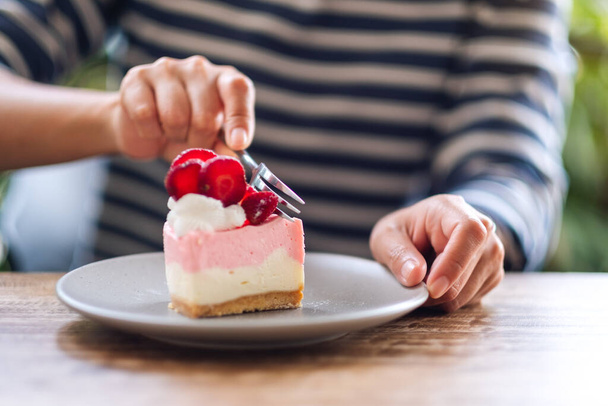 Closeup image of a woman eating a strawberry cheese cake in a plate - 写真・画像