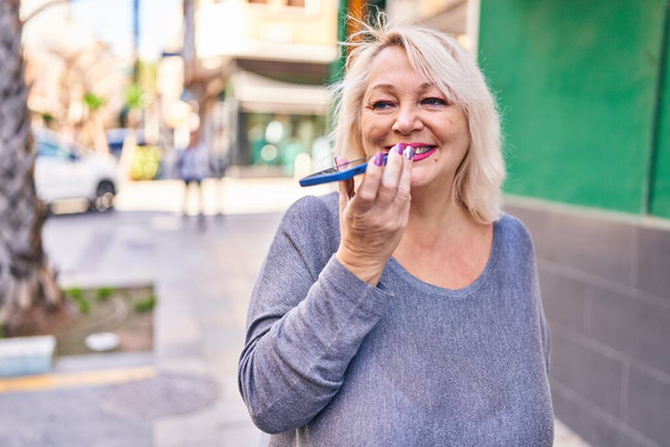 Блондинка середнього віку посміхається впевнено говорити на смартфоні на вулиці
 - Фото, зображення
