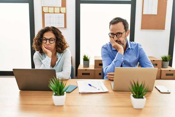 Middle age hispanic woman and man sitting with laptop at the office thinking looking tired and bored with depression problems with crossed arms.  - 写真・画像