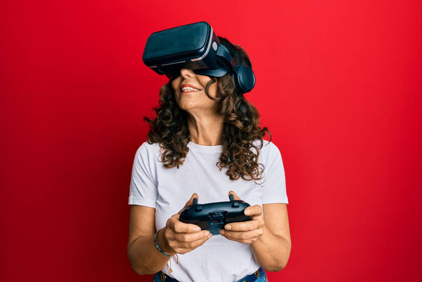 Mujer de mediana edad con gafas de realidad virtual jugando videojuegos 3D, viendo simulación futurista, experiencia emocionada - Foto, Imagen