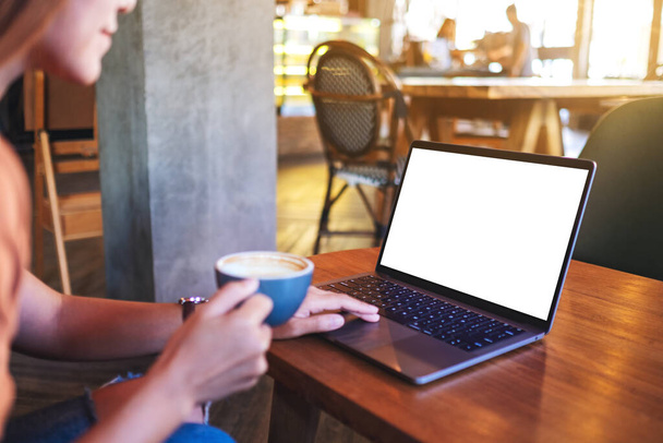 Mockup image of a woman touching on laptop computer touchpad with blank white desktop screen while drinking coffee - 写真・画像