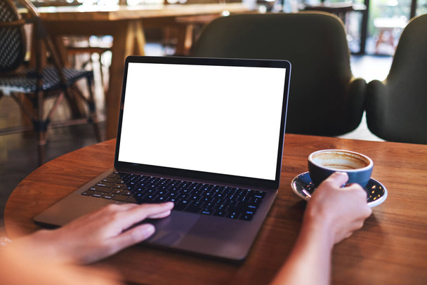 Mockup image of a woman touching on laptop computer touchpad with blank white desktop screen while drinking coffee - Photo, Image