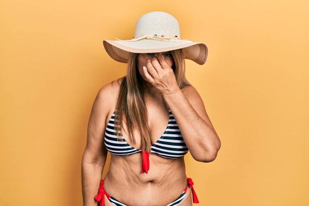 Middle age hispanic woman wearing bikini and summer hat tired rubbing nose and eyes feeling fatigue and headache. stress and frustration concept.  - Foto, immagini