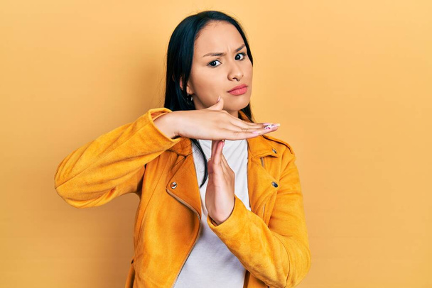 Mooie latino vrouw met neus piercing dragen geel lederen jas doen tijd uit gebaar met de handen, gefrustreerd en ernstige gezicht  - Foto, afbeelding