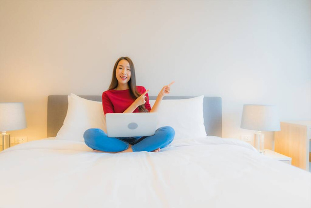 Ritratto bella giovane donna asiatica uso computer portatile sul letto in camera da letto interno - Foto, immagini