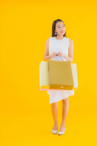 Portrait beautiful young asian woman with shopping bag from retails department store on yellow isolated background - Фото, изображение