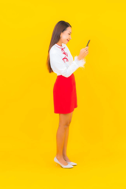Porträt schöne junge asiatische Frau mit Smartphone auf gelbem Hintergrund - Foto, Bild