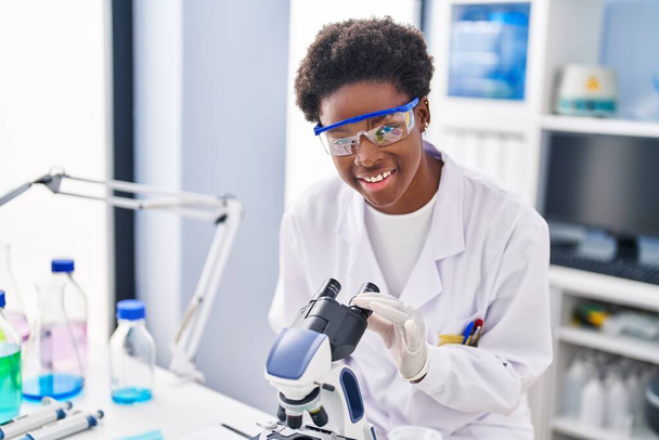 Femme afro-américaine portant un uniforme de scientifique au microscope au laboratoire - Photo, image