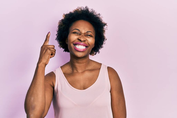Молода афроамериканська жінка, одягнена в звичайну сорочку без рукавів, вказує пальцем вгору з успішною ідеєю. схвильований і щасливий. № 1.  - Фото, зображення
