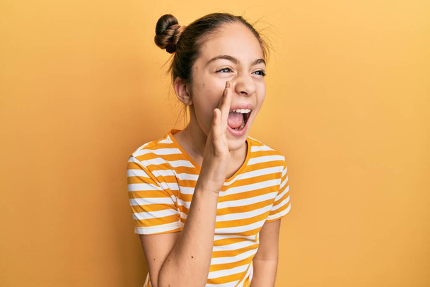Beautiful brunette little girl wearing casual striped t shirt shouting and screaming loud to side with hand on mouth. communication concept.  - Fotó, kép