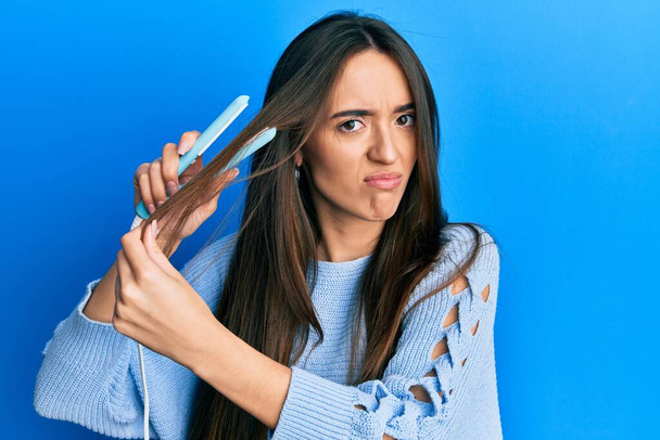 Young hispanic girl holding hair straightener skeptic and nervous, frowning upset because of problem. negative person.  - Foto, Imagen