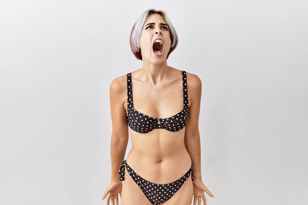 Young beautiful woman wearing swimsuit over isolated background angry and mad screaming frustrated and furious, shouting with anger. rage and aggressive concept.  - Fotoğraf, Görsel