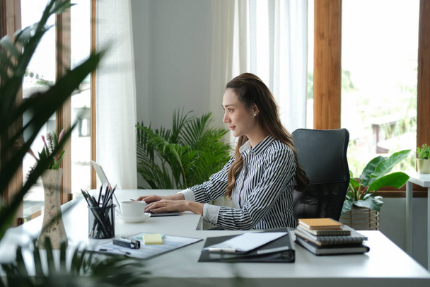 Vista lateral da mulher de negócios concentrada que trabalha com computador portátil no escritório moderno brilhante. - Foto, Imagem