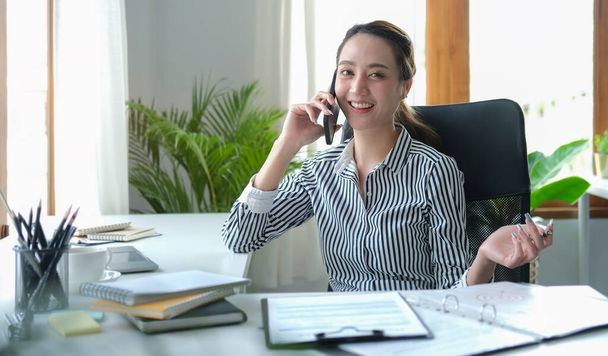 Empresaria asiática revisando informes financieros y hablando por teléfono móvil. - Foto, Imagen