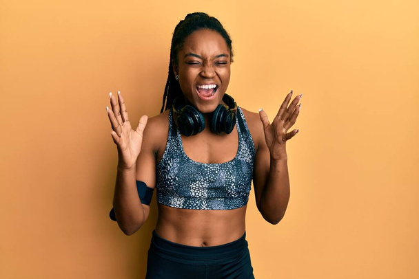 African american woman with braided hair wearing sportswear and arm band celebrating mad and crazy for success with arms raised and closed eyes screaming excited. winner concept  - Fotoğraf, Görsel