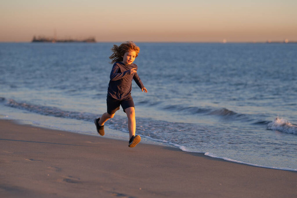 Sahilde oynayan çocuklar. Çocuklar yaz tatilinde denizde oynarlar. Kum ve su eğlencesi, güneş koruması. Okyanus kıyısında koşan ve zıplayan küçük bir çocuk. Küçük koşucu egzersiz yapıyor.. - Fotoğraf, Görsel