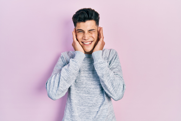 Junger hispanischer Mann in lässiger Kleidung, der die Ohren mit den Fingern mit genervtem Gesichtsausdruck vor lauter Musik verdeckt. Gehörloses Konzept.  - Foto, Bild