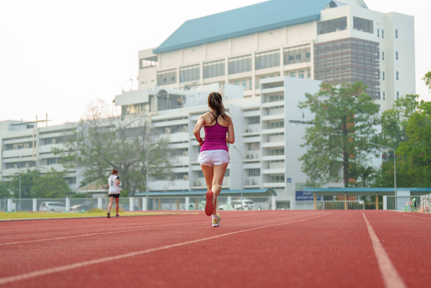 asian women middle aged running during sunny morning on stadium track - Фото, изображение
