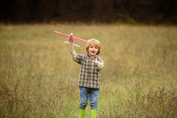 Kid having fun with toy airplane in field. Little boy with wooden plane, boy wants to become pilot and astronaut. Happy child play with toy airplane. Kids pilot dreams of flying on field. - Foto, Bild