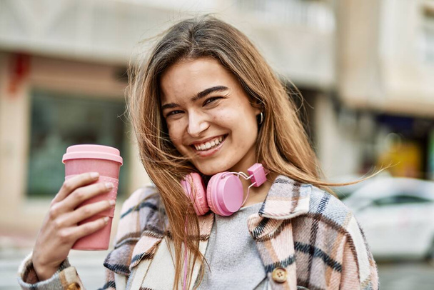 Młoda blondynka w słuchawkach z kawą na ulicy - Zdjęcie, obraz