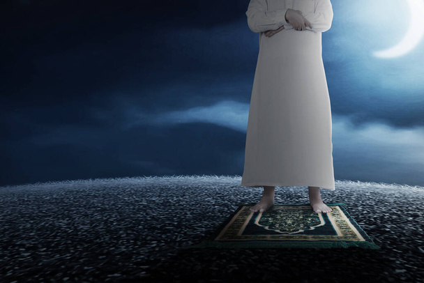 Close up view of a Muslim man in a praying position (salat) on a prayer rug with a night scene background - Foto, imagen
