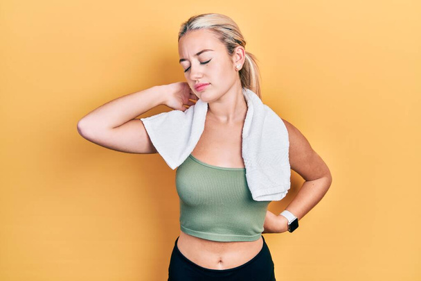 Young blonde girl wearing sportswear and towel suffering of neck ache injury, touching neck with hand, muscular pain  - Fotó, kép