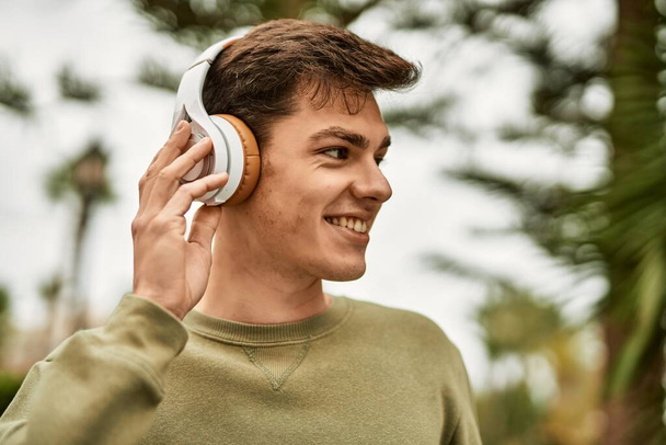 Jeune homme hispanique souriant heureux en utilisant des écouteurs à la ville. - Photo, image