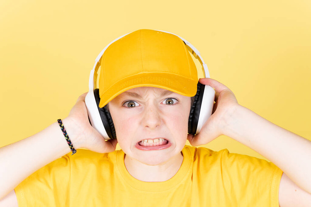 Επιθετική θυμωμένος αγόρι ακούγοντας ροκ μουσική στα ακουστικά και κοιτάζοντας κατ 'ευθείαν στην κάμερα. Άγχος στην έννοια της παιδικής ηλικίας - Φωτογραφία, εικόνα