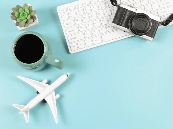 Top view or flat lay of computer keyboard, blue cup of black coffee, airplane model  and succulent plant pot  on blue  background with copy space. Traveling concept. - Photo, image