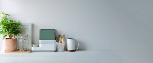 Minimal workspace with picture frame, book, coffee cup and pencil holder on white table. Copy space for your advertising text. - Zdjęcie, obraz