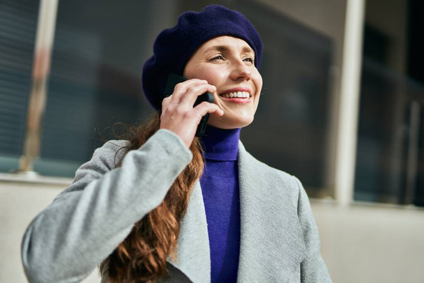 Fiatal szőke nő mosolyog boldog beszél az okostelefonon a városban. - Fotó, kép