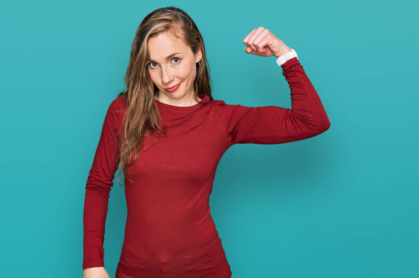 Mujer rubia joven que usa ropa casual persona fuerte que muestra el músculo del brazo, confiado y orgulloso de poder  - Foto, Imagen