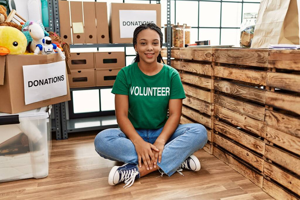 Junge Afroamerikanerin im freiwilligen T-Shirt am Spendenstand mit einem fröhlichen und kühlen Lächeln im Gesicht. Glück gehabt.  - Foto, Bild