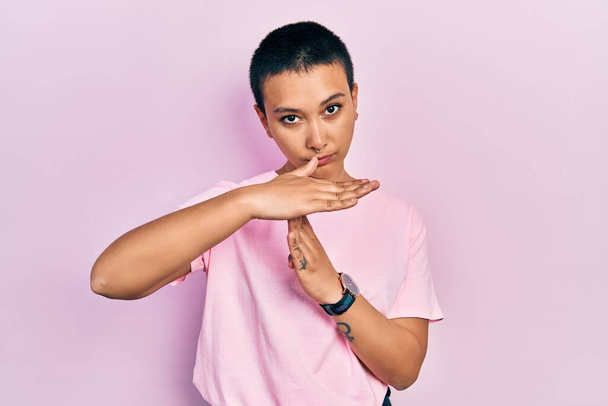 Beautiful hispanic woman with short hair wearing casual pink t shirt doing time out gesture with hands, frustrated and serious face  - Photo, Image