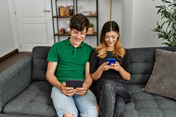 Jeune couple caucasien souriant heureux en utilisant touchpad et smartphone à la maison. - Photo, image
