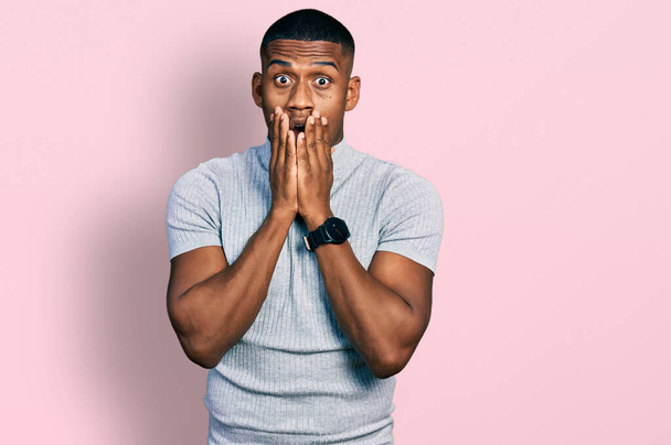 Young black man wearing casual t shirt afraid and shocked, surprise and amazed expression with hands on face  - Photo, image