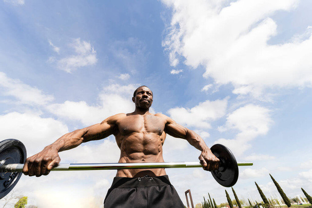 Afrikanisch-amerikanischer männlicher Athlet beim Training im Freien. Afrikanische Athleten beim Training im Park. ein muskulöser junger schwarzer Mann, der entschlossen ist, die Stange zu heben. Gesundheits- und Fitnesskonzept - Foto, Bild