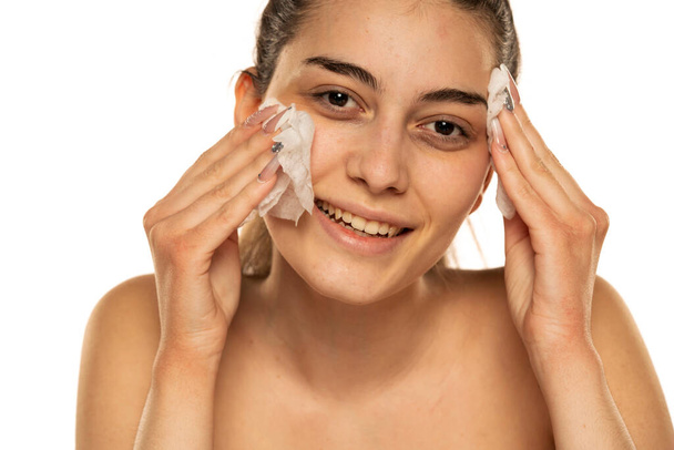onnellinen nuori nainen puhdistaa kasvonsa kostealla pyyhkeellä valkoisella taustalla - Valokuva, kuva