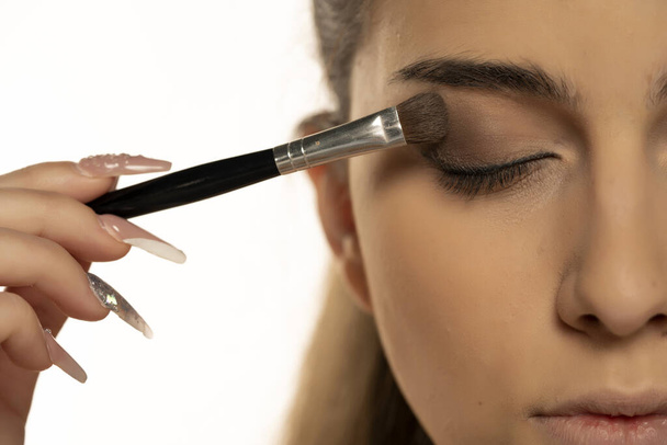 close up of a young woman applying eye shadow with a brush on a white background - Φωτογραφία, εικόνα